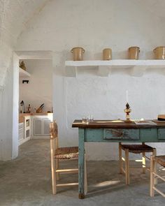 an old table and two chairs in a room with white walls, open shelving