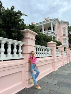 a woman leaning against the side of a pink building with balconies on it