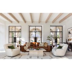 a living room filled with lots of furniture next to tall windows and wooden beams on the ceiling