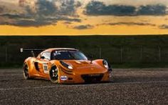 an orange sports car parked on the side of a road in front of a cloudy sky