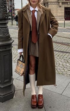 a woman in a coat and tie is standing on the sidewalk