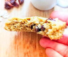 a hand holding an oatmeal cookie with raisins in the background