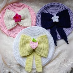 three crocheted hats with bows on them sitting on top of a white blanket