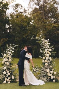 a bride and groom kissing in front of an arch of white roses at their wedding