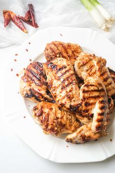 grilled chicken on a white plate next to garlic and red pepper florets