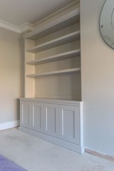 an empty living room with built - in bookcases and a large clock on the wall