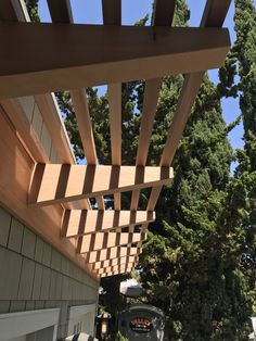 a wooden pergoline on the side of a building with trees in the background