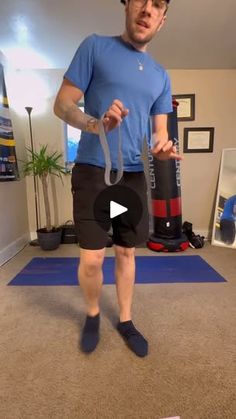 a man in blue shirt and black shorts holding a pair of scissors while standing on a yoga mat