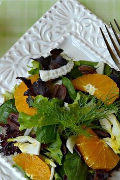 a salad with oranges, lettuce and other vegetables on a white plate