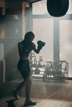 a woman standing in a gym with a punching glove on her chest and wearing black shorts