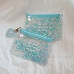 two clear bags with blue and white sequins on them, one has a keychain that says i believe all your moments will shine