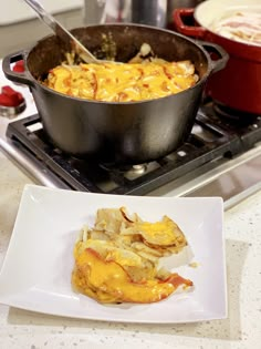 a pan filled with macaroni and cheese sitting on top of a stove next to a white plate