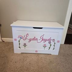 a white toy box with flowers painted on the side and name written in pink letters