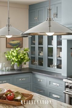 a kitchen with blue cabinets and two hanging lights over the counter top, along with a basket of fruit