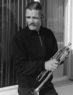 a man sitting on a window sill with a trumpet in his hand and looking at the camera