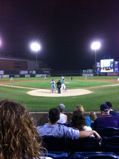 people watching a baseball game at night in an empty stadium with lights on the stands