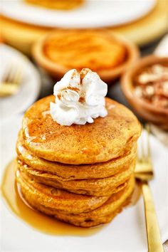 a stack of pancakes with whipped cream on top sitting on a plate next to other plates