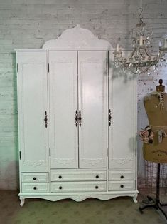 an antique white armoire with chandelier and dress form next to it in a room