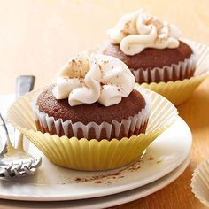 two chocolate cupcakes with white frosting on a plate next to silverware