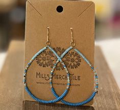 a pair of blue beaded hoop earrings sitting on top of a wooden table next to a cardboard box