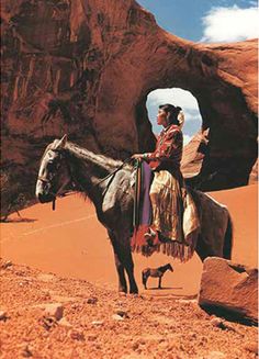 a man riding on the back of a brown horse next to a rock formation and a small bird