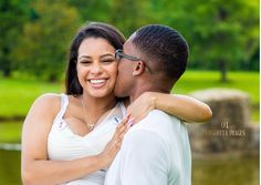 a man and woman embracing each other in front of a pond