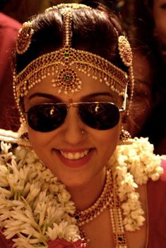 a woman in sunglasses and headdress with flowers around her neck smiling at the camera