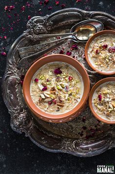 three bowls filled with oatmeal on top of a metal tray next to spoons