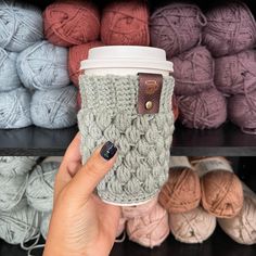 a woman holding up a coffee cup in front of some balls of yarn