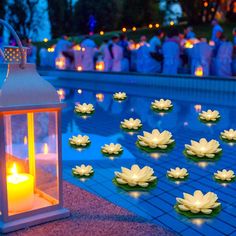 candles are floating on the water in front of a lighted lantern and lily pad decorations