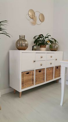 a white dresser with wicker baskets on top and two potted plants on top