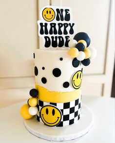 a white cake with black and yellow decorations on it's side, decorated with smiley faces