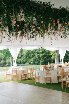 the tables are set up with white linens and flowers hanging from the ceiling above them