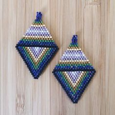 two handmade beaded ornaments hanging on a wooden surface, one is blue and the other is green