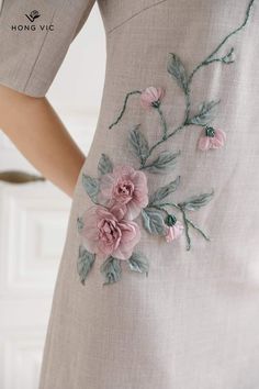 a woman wearing a dress with pink flowers on the side and green leaves on the back