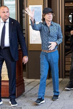 two men in suits and ties are walking down the street with one man waving to someone