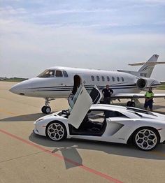 a white sports car sitting on top of an airport tarmac with a plane in the background