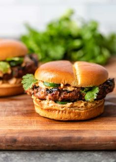 two burgers with meat and lettuce on a cutting board