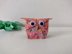 an origami owl sitting next to some green leaves