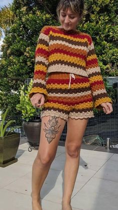 a woman with tattoos on her leg wearing a striped sweater and shorts, while standing in front of a potted plant