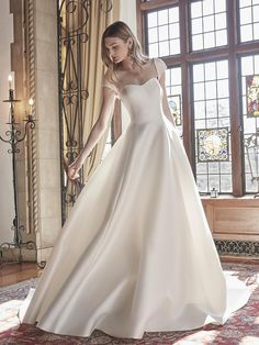 a woman in a white wedding dress is standing on a rug and looking down at the floor