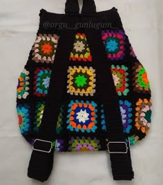 a crocheted backpack hanging from a hook on a white wall with black straps