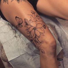 a woman's arm with flowers and butterflies tattooed on her left leg, sitting on a bed