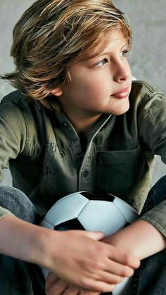 a young boy sitting on the ground holding a soccer ball