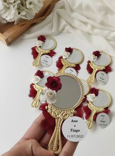 a hand holding a mirror with red roses on it and some tags attached to the mirror