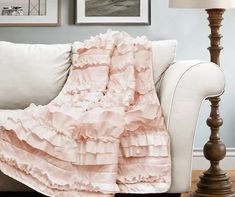 a white couch with a pink ruffled blanket on it's back in front of two framed pictures