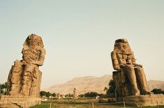 two large statues sitting in the middle of a field