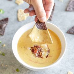 a hand dipping a tortilla chip into a bowl of dip with chips on the side