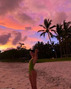 a woman in a green bathing suit standing on the beach with palm trees behind her