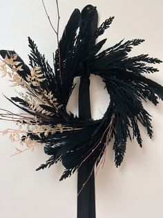 a black and white wreath hanging on the side of a wall with dried plants in it